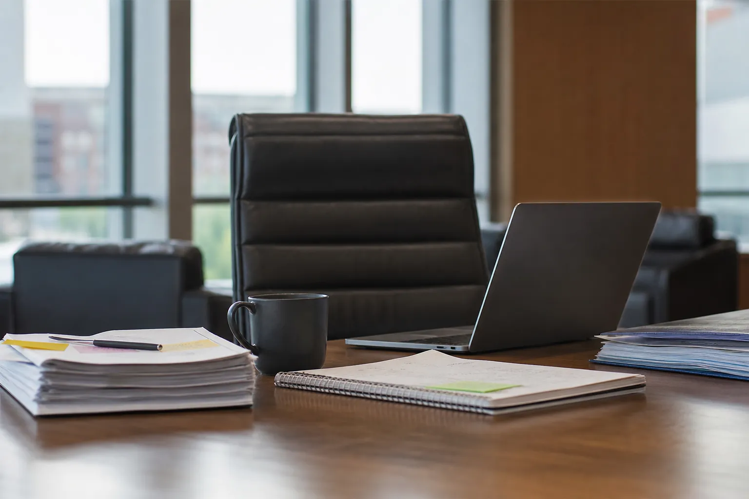 Vacant CFO Desk During a Leadership Transition Vacant executive chair behind a desk with an open laptop, coffee mug, notebook, and stacks of financial documents.